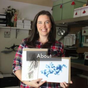 Photo of Marnie in her studio, holding two of her artworks.