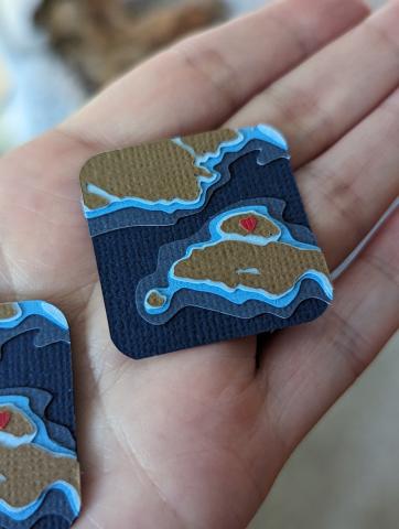 Small, layered paper art piece showing an island off the coast of the mainland.